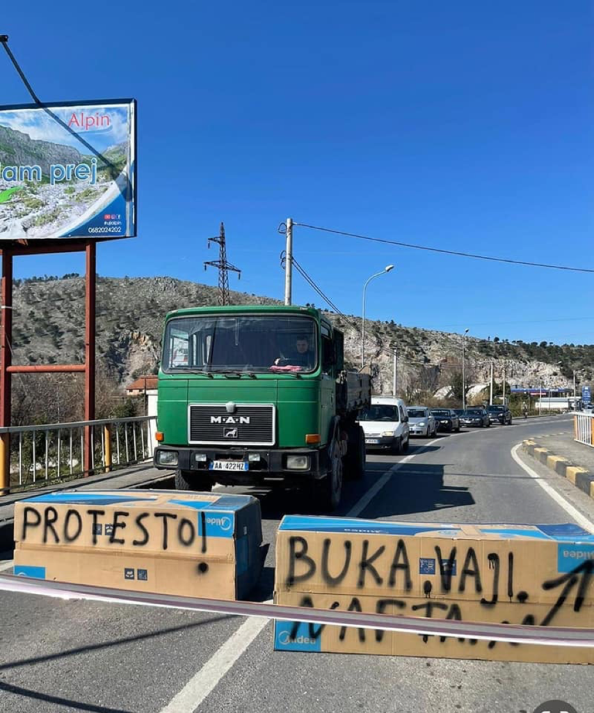 A truck stands in front of a sign "Protest for your bread" in Albania.