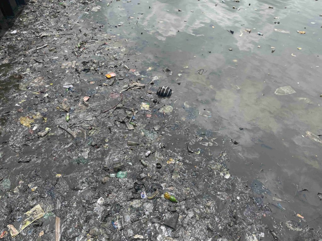 Exposed waterbed shows trash and layers of wet soot in Nigeria