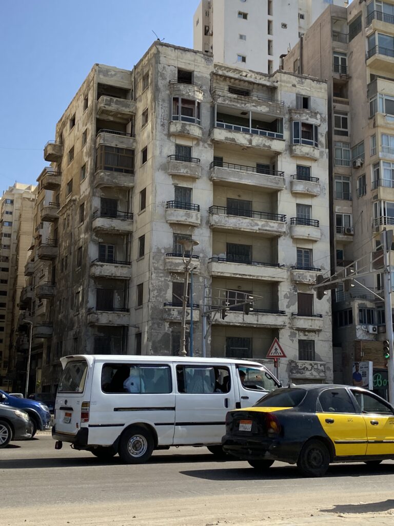 A building in Alexandria with obvious cracks and damage, while cards drive by on the street