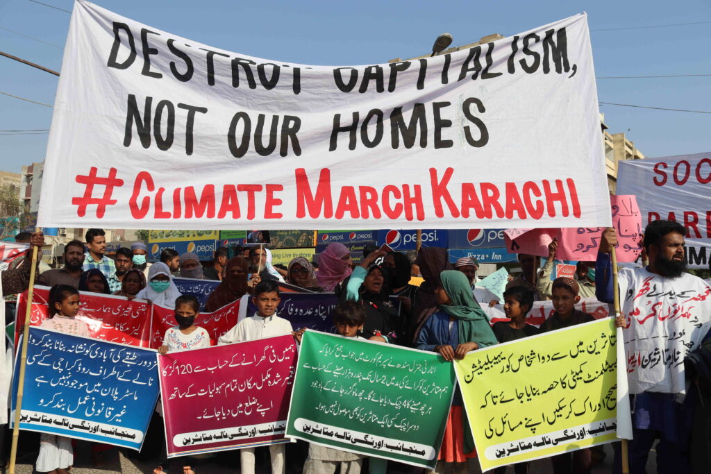 Children and adults at a protest with signs in Urdu as well as English, reading "Destroy capitalism, not our home" #Climate March Karachi