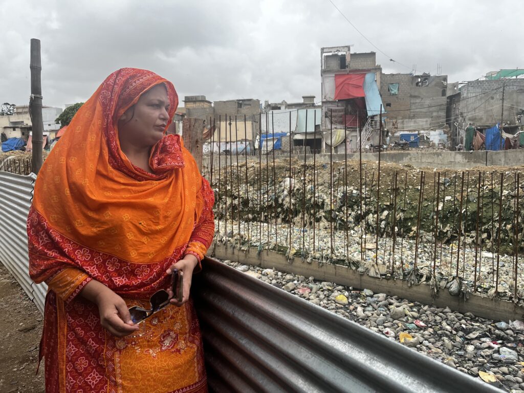Erum Yasmeen, dressed in an orange dress and matching hijab and holding her sunglasses, looks over where her home used to be.