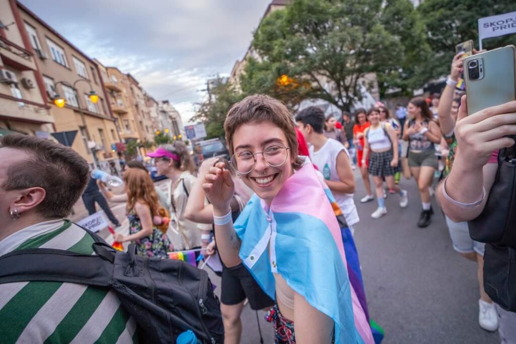 Leo Popovic, smiling and draped in a flag, attends a Pride parade