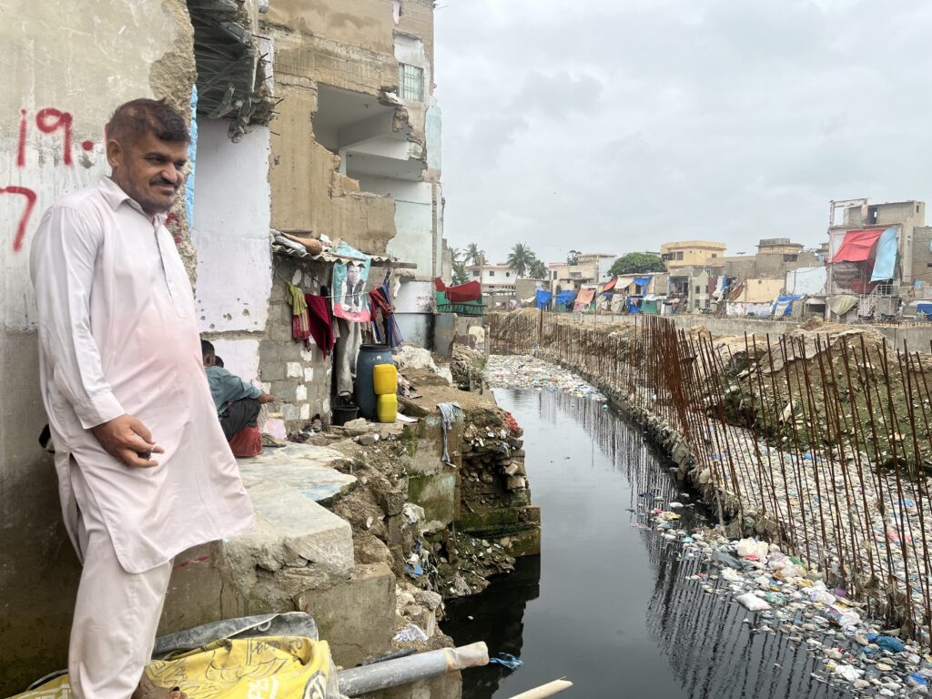 A man stands overlooking a waterway filled with trash in a partially demolished house