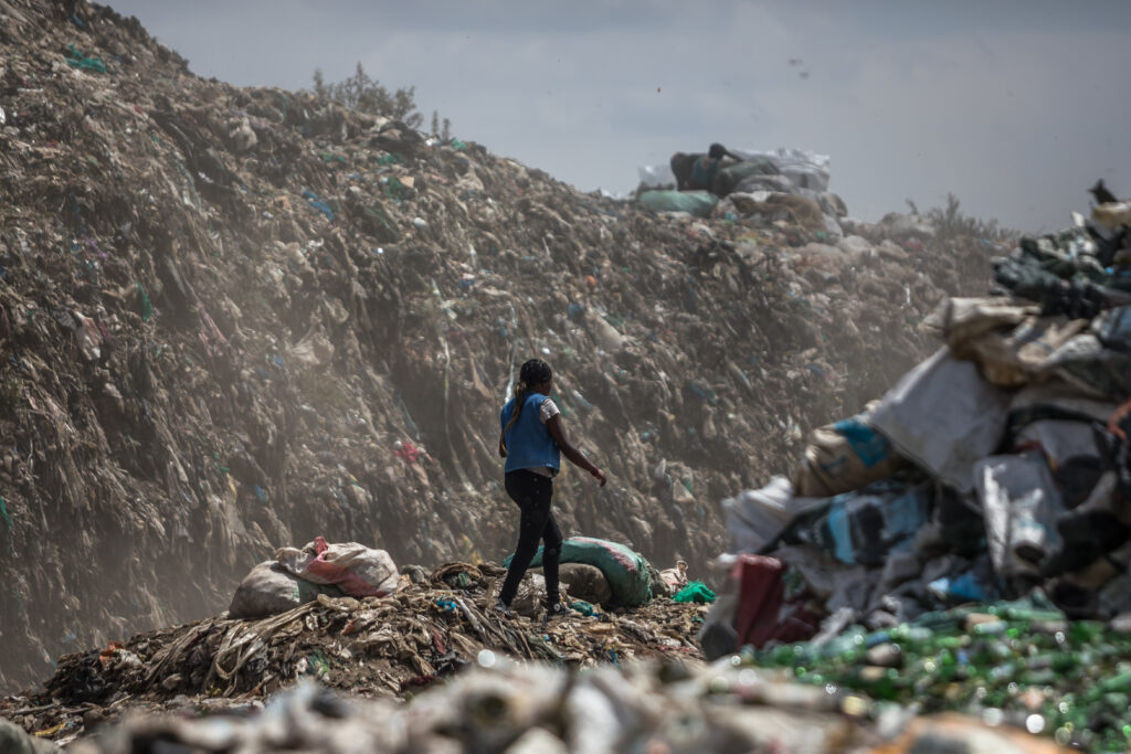 , a woman walks under a mountain of waste at the Dandora’s dumpsite