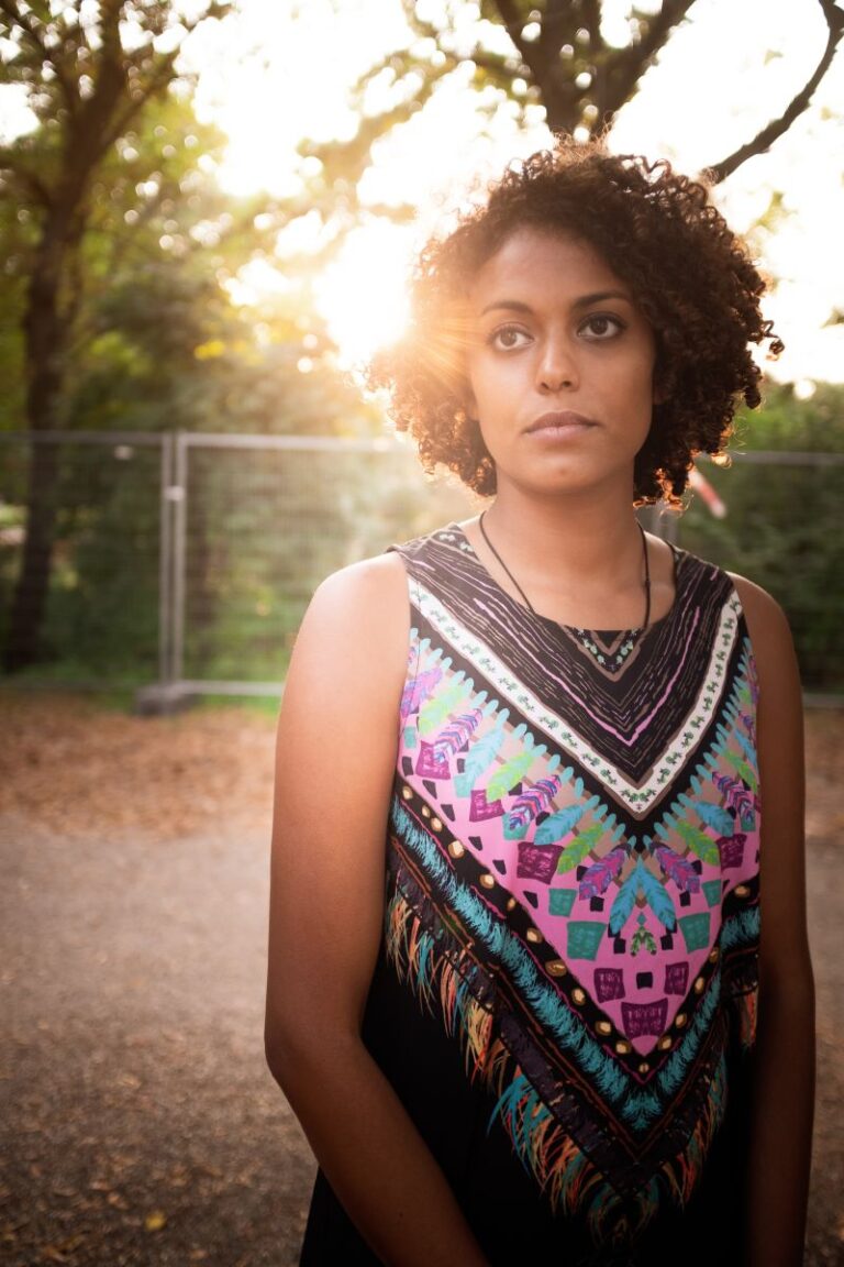 A woman in a multi-colored shirt stands in the sun, Wafaa Albadry.