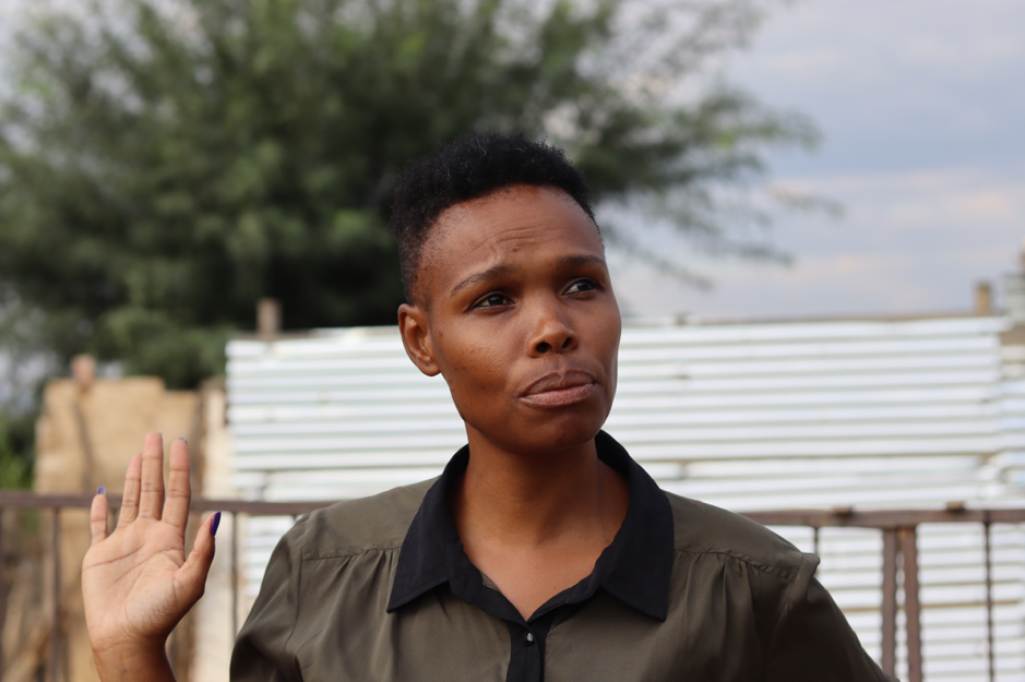 A woman stands with her hand up in front of a corrugated metal rooftop