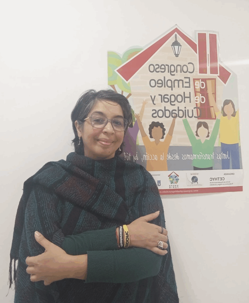 Edith Espínola smiles at the camera at CETHYC in Madrid in February 2025, with the official sign from the 2016 First Congress of Domestic and Care Work in the background. Photo: Edith Espínola