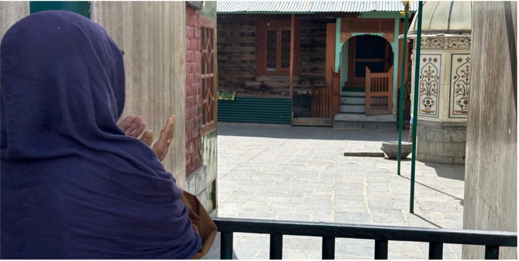 A woman in a purple headscarf is shown from the back at the shrine of Sufi saint Khawaja Masood Wali in Pampore, Pulwama district, Kashmir.